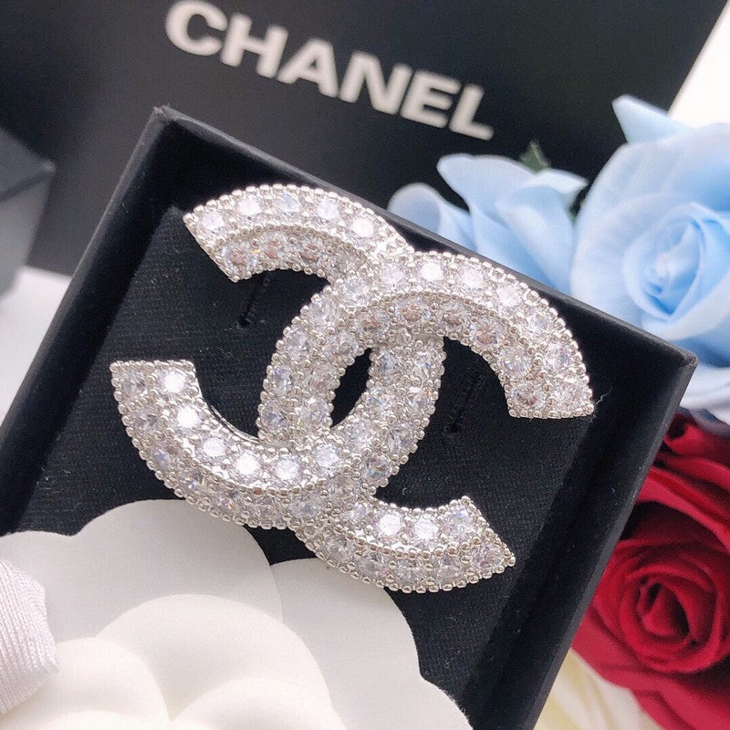 Chanel brooch with crystals on a black box with Chanel branding, surrounded by roses.